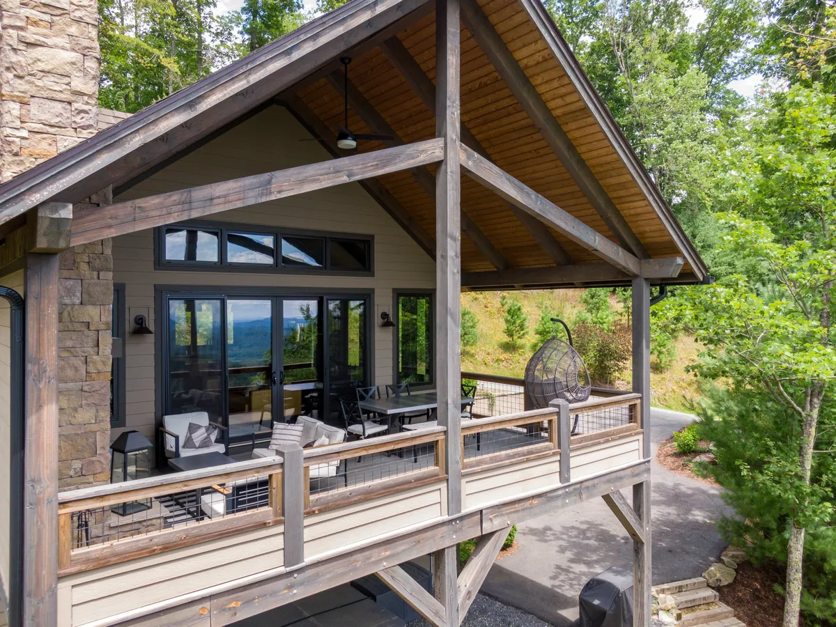 This image captures a spacious wooden deck adorned with a hanging chair and bordered by large windows, all surrounded by lush trees. The tranquil outdoor setting is perfect for enjoying mountain views and outdoor gatherings, directly reflecting the experience of morning coffee with breathtaking vistas as described in the section.