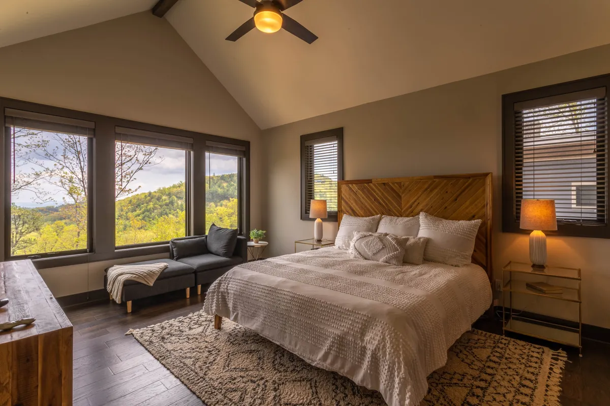 A tranquil bedroom featuring a cozy bed positioned near large windows that offer unobstructed mountain views. The room includes a stylish seating area, soft natural light, and decor that emphasizes a calm, inviting atmosphere—perfect for relaxing or reading.