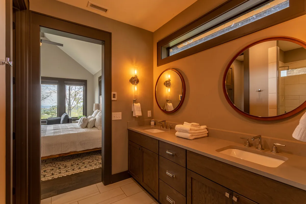 A bright, modern bathroom with double mirrors, a sleek vanity topped with towels, and natural light streaming in. The soothing color palette and uncluttered surfaces evoke a spa-like ambiance, ideal for morning routines or unwinding in the evening.