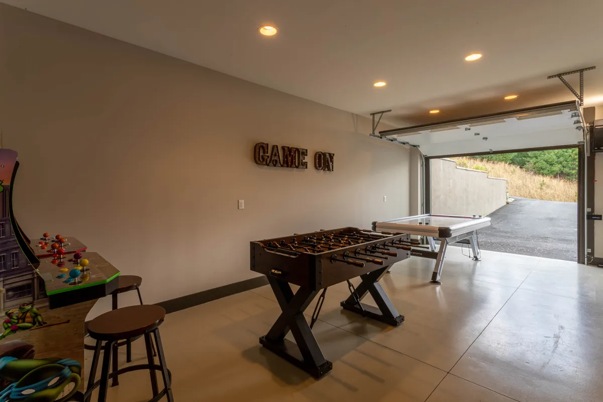 A vibrant game room featuring a foosball table, air hockey table, arcade machine, and a bright 'GAME ON' sign. The space is designed for playful interaction, with comfortable lighting and open floor space for movement.