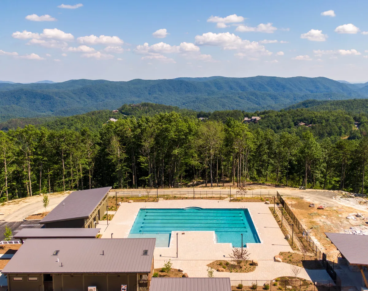 An exterior view of the community swimming pool, set against sweeping mountain scenery and surrounded by wooded areas and modern buildings. The pool area is tranquil yet vibrant, designed for both relaxation and social gatherings.