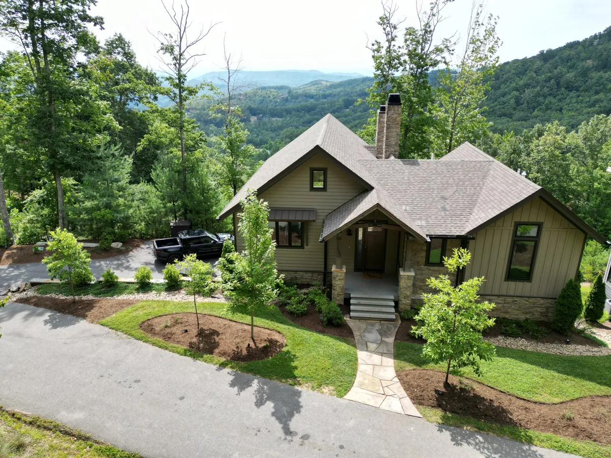 A welcoming exterior shot of the home set amid tall trees, with a pathway leading to the entrance. The house is nestled in its serene mountain surroundings, and the inviting porch hints at leisurely mornings or evenings spent outdoors. The overall setting is tranquil and encourages exploration of both the property and its natural environment.