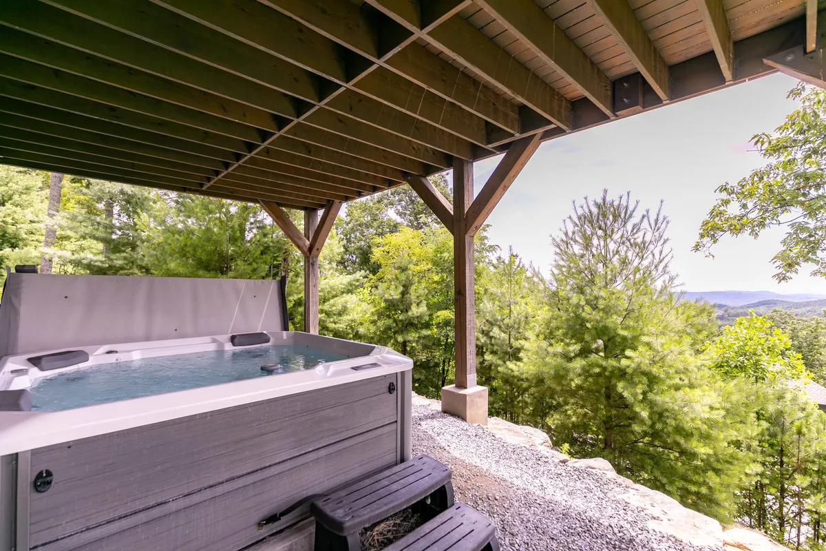 An outdoor hot tub nestled beside a wooden structure with expansive scenic views. The setting is tranquil, perfect for soaking and enjoying sunset or stargazing after a day of adventure.